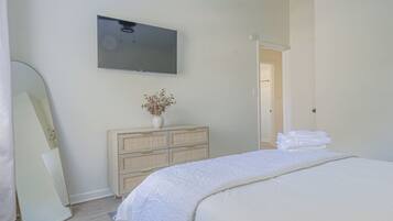A bedroom with a bed, a dresser, a mirror, a television, and a door leading to another room.