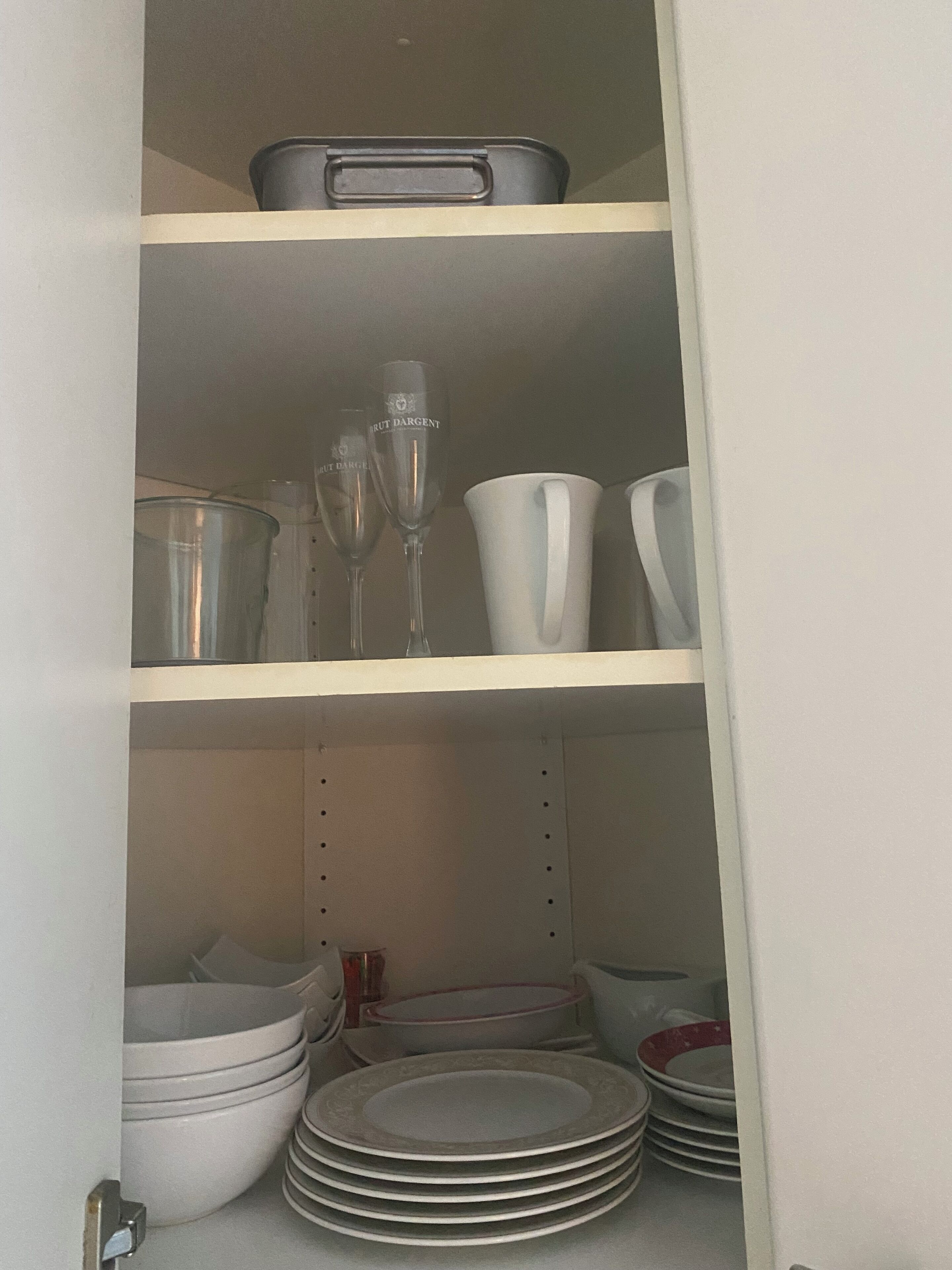 Un mueble de cocina con estantes que contienen distintos utensilios de cocina, como platos, cuencos y copas de vino.