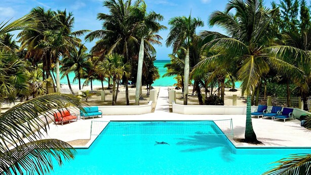 A pool with a heart-shaped design, surrounded by palm trees and lounge chairs, with a clear sky above.