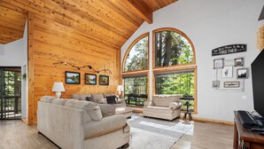 A spacious living room with wooden ceiling beams, large arched windows, and a cozy seating area with two sofas and a coffee table.