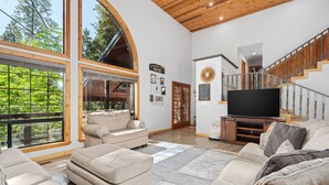 A spacious living room with large windows, a staircase, and a flat-screen TV.