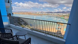 Un balcon offrant une vue sur une étendue d’eau, un paysage urbain lointain et des montagnes.