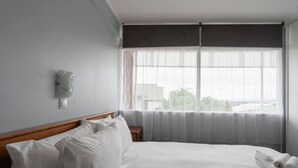 Een hotelkamer met een groot bed, een nachtkastje, een wandlamp en een raam met dunne gordijnen.