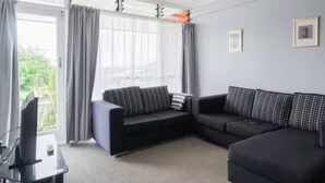 Een moderne woonkamer met een hoekbank, een flatscreen televisie en een groot raam met gordijnen.