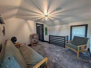 Una habitación acogedora con cama, una silla, una mesita, una estantería y una lámpara en el techo.