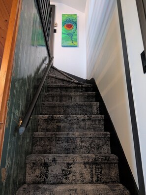 Una escalera con alfombra texturizada y barandilla, que conduce a una habitación con un cuadro en la pared.