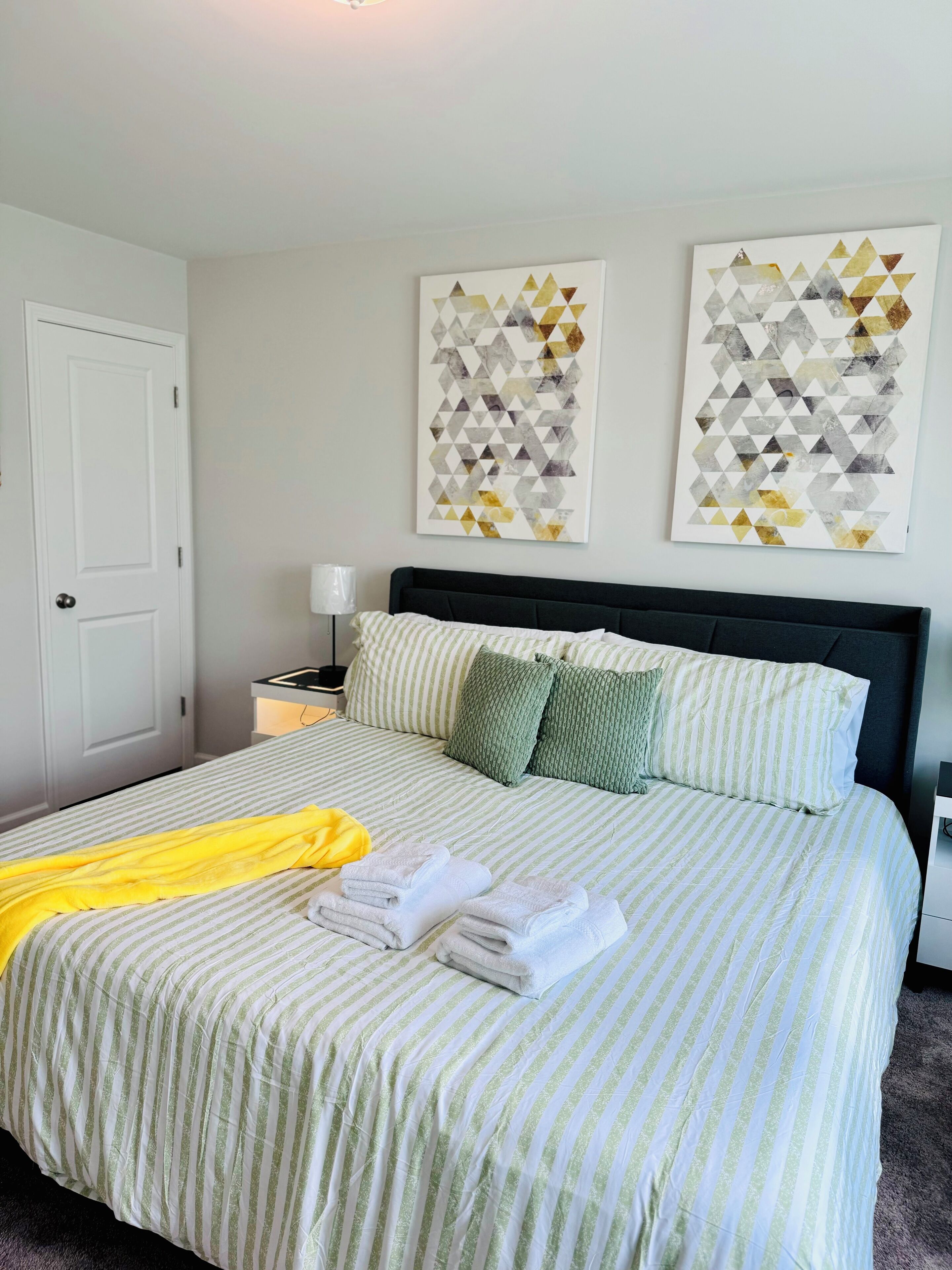 A neatly made bed with striped bedding, a yellow towel, and folded towels. There are two wall-mounted artworks above the bed.