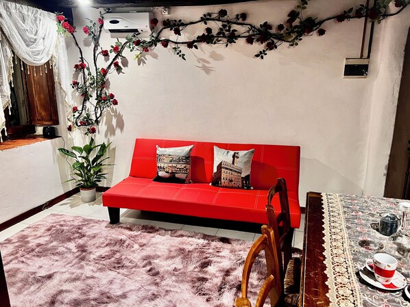 A red sofa with two pillows, a pink furry rug, a wooden chair, a lace tablecloth, and a small table with a teapot and cups. - A romantic mini apartment in the heart of Florence with a great location! (Firenze)