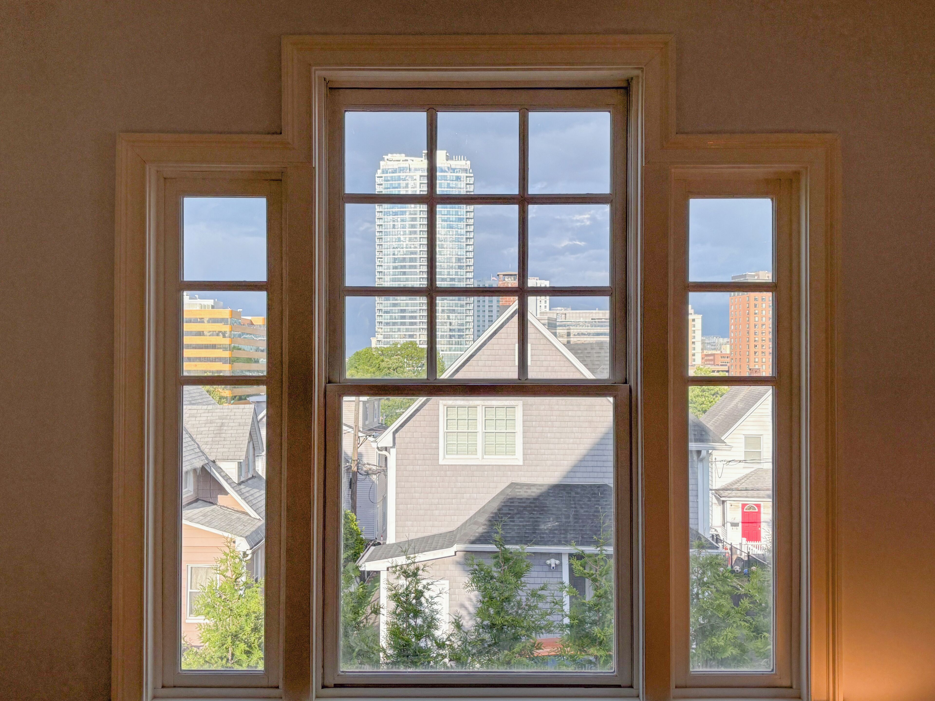 A window with a view of a cityscape, including high-rise buildings and residential houses.