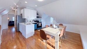 Una cocina moderna con armarios blancos, una isla central y un comedor con mesa y sillas de madera.