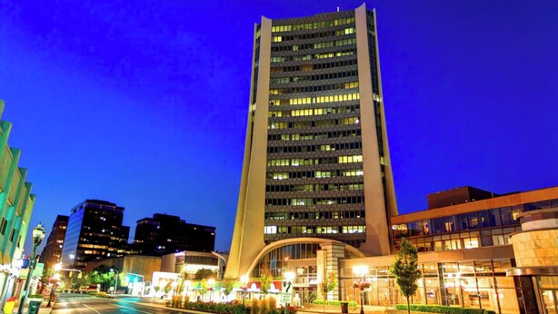 Un moderno edificio de gran altura con una entrada curva, rodeado de calles bien iluminadas y otros edificios.