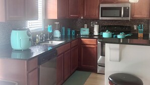 A modern kitchen with wooden cabinets, a stainless steel microwave, a coffee maker, and a teal-colored toaster.
