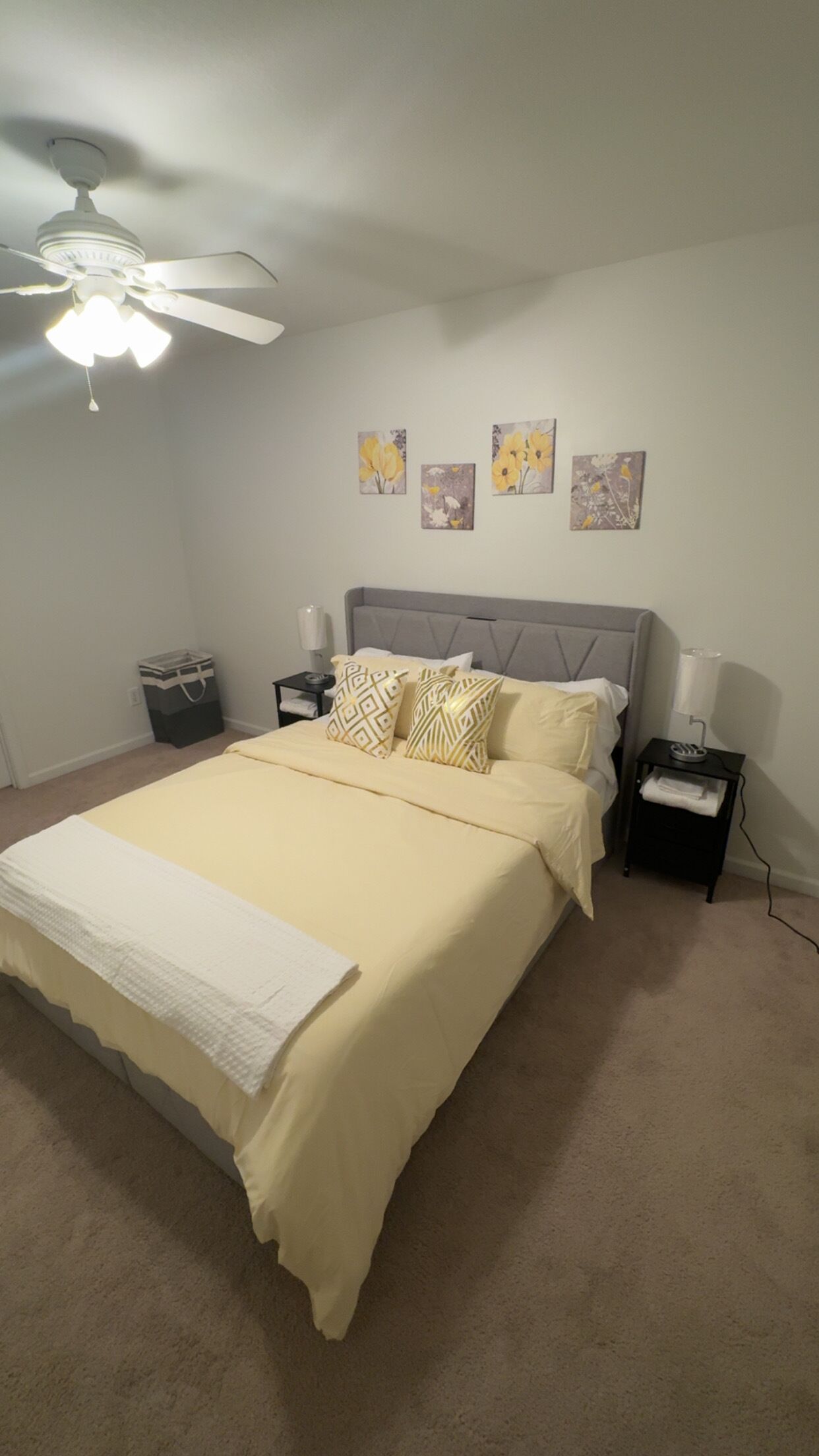 A bedroom with a bed, nightstands, a ceiling fan, and wall art.