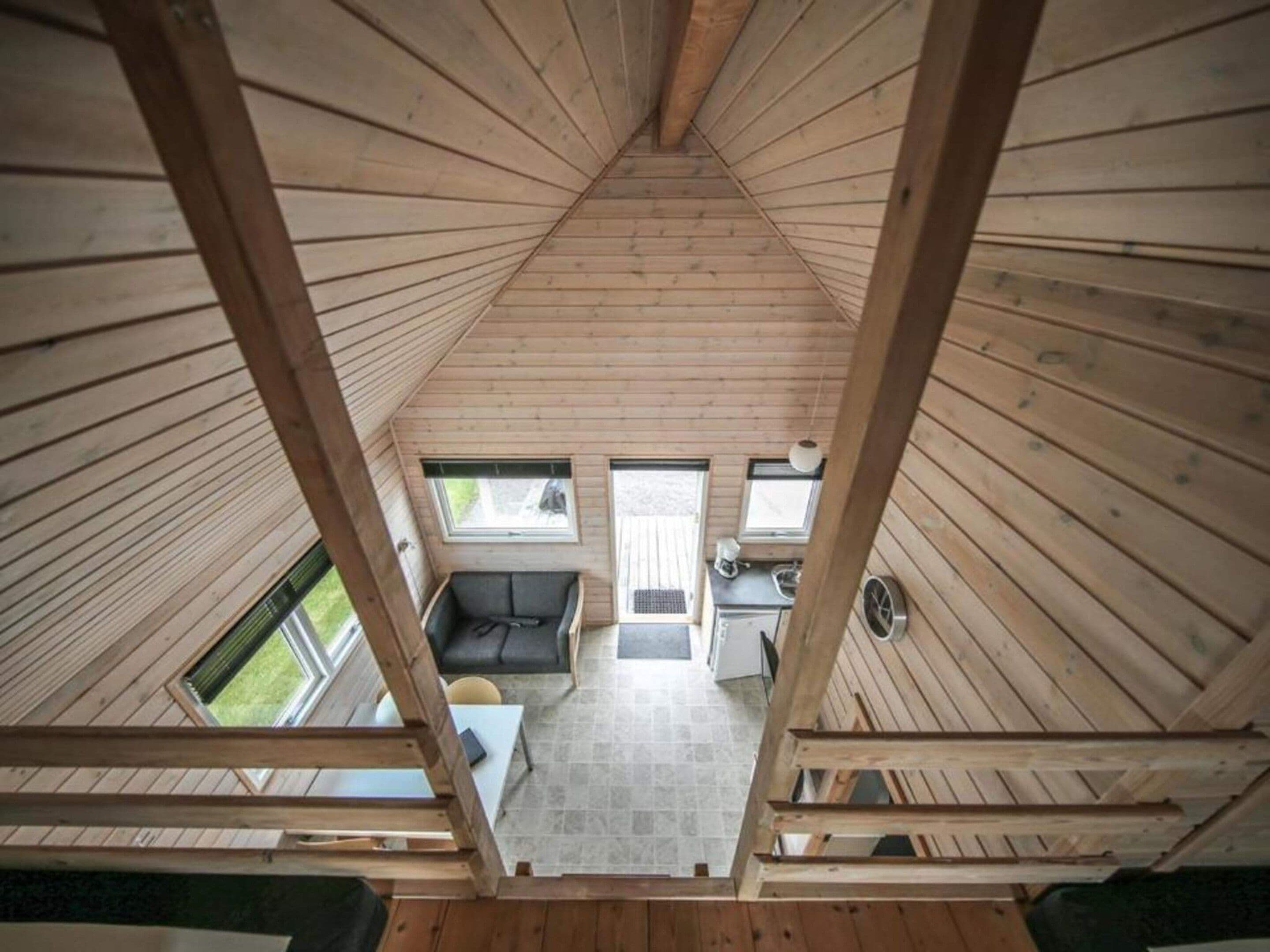 A high-ceilinged wooden cabin with a loft bedroom, a dining area, and a kitchen.