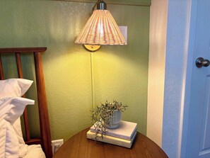 A bedside table with a lamp, a potted plant, and a stack of books. - The Citrus Suite, Near UF, Shands, Downtown (Gainesville)