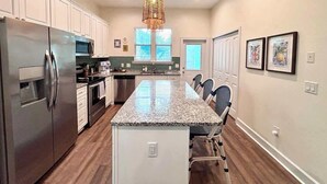 A modern kitchen with a central island, stainless steel appliances, and a hanging light fixture. - The Citrus Suite | Upscale Near UF/Downtown (Gainesville)