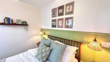 A neatly made bed with pillows, a bedside lamp, and a wall-mounted shelf with books and a small plant.