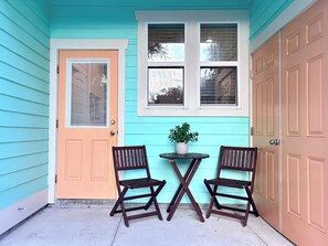 A two-door garage with a teal siding exterior, a small table with a potted plant, and two wooden chairs. - The Citrus Suite, Near UF, Shands, Downtown (Gainesville)