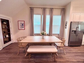 A dining area with a wooden table and bench, a refrigerator, and a window with curtains. - The Citrus Suite, Near UF, Shands, Downtown (Gainesville)