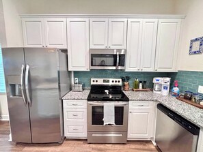 A kitchen with white cabinets, stainless steel appliances, a granite countertop, and a tiled backsplash. - The Citrus Suite, Near UF, Shands, Downtown (Gainesville)