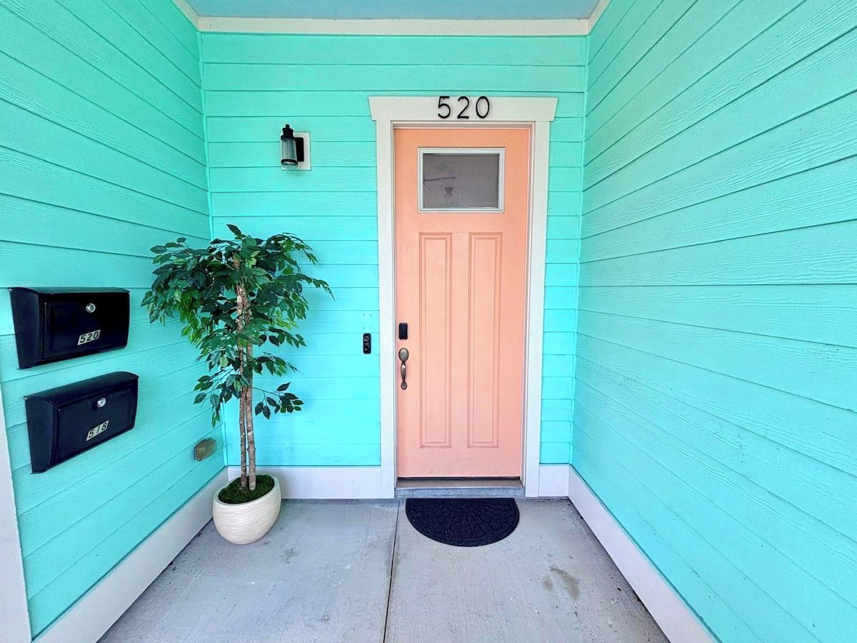 Une maison turquoise avec une porte de couleur pêche, une boîte aux lettres et un pot de fleurs.