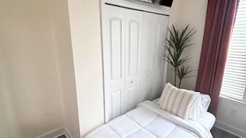 Un dormitorio con una cama, un armario blanco, un televisor sobre el armario y una ventana con cortinas.