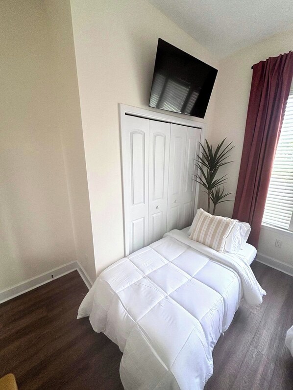 Un dormitorio con una cama, un armario blanco, un televisor sobre el armario y una ventana con cortinas.