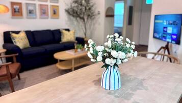 Una mesa de comedor con un florero, un sofá, una mesa de centro y un televisor al fondo.