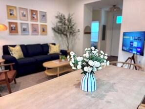 A dining table with a vase of flowers, a sofa, a coffee table, and a television in the background. - The Citrus Suite, Near UF, Shands, Downtown (Gainesville)