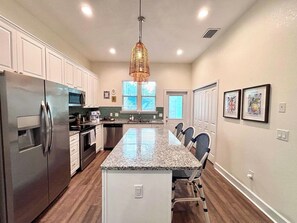 A modern kitchen with a central island, stainless steel appliances, and a hanging light fixture.