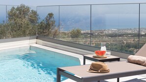 A rooftop pool with clear blue water, a glass of water, a slice of watermelon, and a hat on a lounge chair. - Villa Santa Irini 2 - With Heated Pool (Agia Eirini)