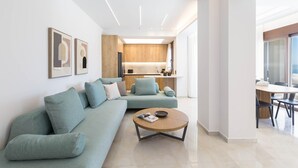 A modern living room with a light blue sofa, a round coffee table, and a kitchen area in the background. - Villa Santa Irini 2 - With Heated Pool (Agia Eirini)