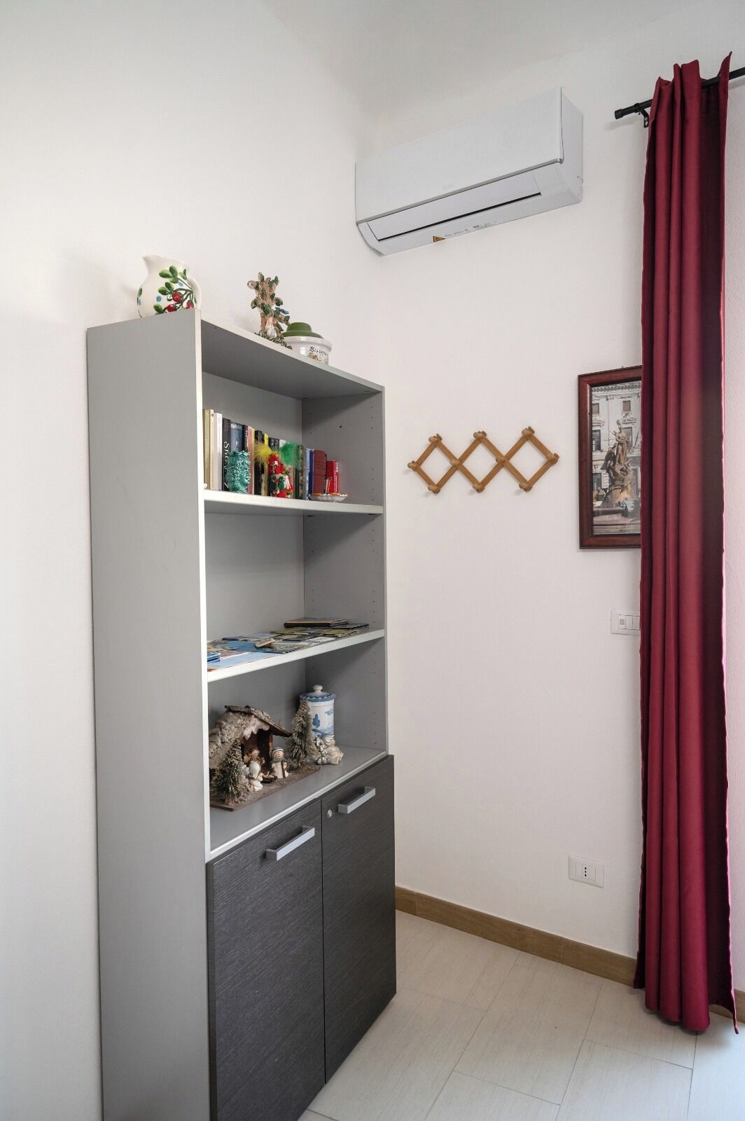 A room with a grey bookshelf, a red curtain, and a wall-mounted air conditioner.