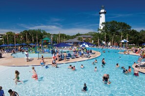 A large outdoor swimming pool with multiple lanes, surrounded by lounge chairs and umbrellas, and a lighthouse in the background.