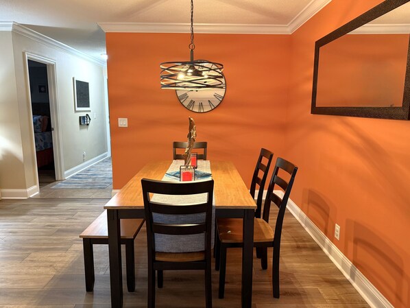 A dining area with a wooden table and chairs, a unique pendant light, and a clock on the wall.