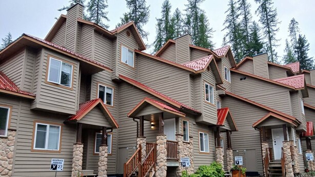 A multi-story building with stone pillars, wooden railings, and a parking area. - Ski-In Stone Creek Condo - Hot Tub - 3 bedroom - Pet Friendly (Fernie)