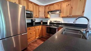 A kitchen with wooden cabinets, stainless steel appliances, a microwave, a stove, and a sink. - Ski-In Stone Creek Condo - Hot Tub - 3 bedroom - Pet Friendly (Fernie)