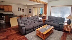 A living room with a gray sofa, a wooden coffee table, and a kitchen in the background. - Ski-In Stone Creek Condo - Hot Tub - 3 bedroom - Pet Friendly (Fernie)