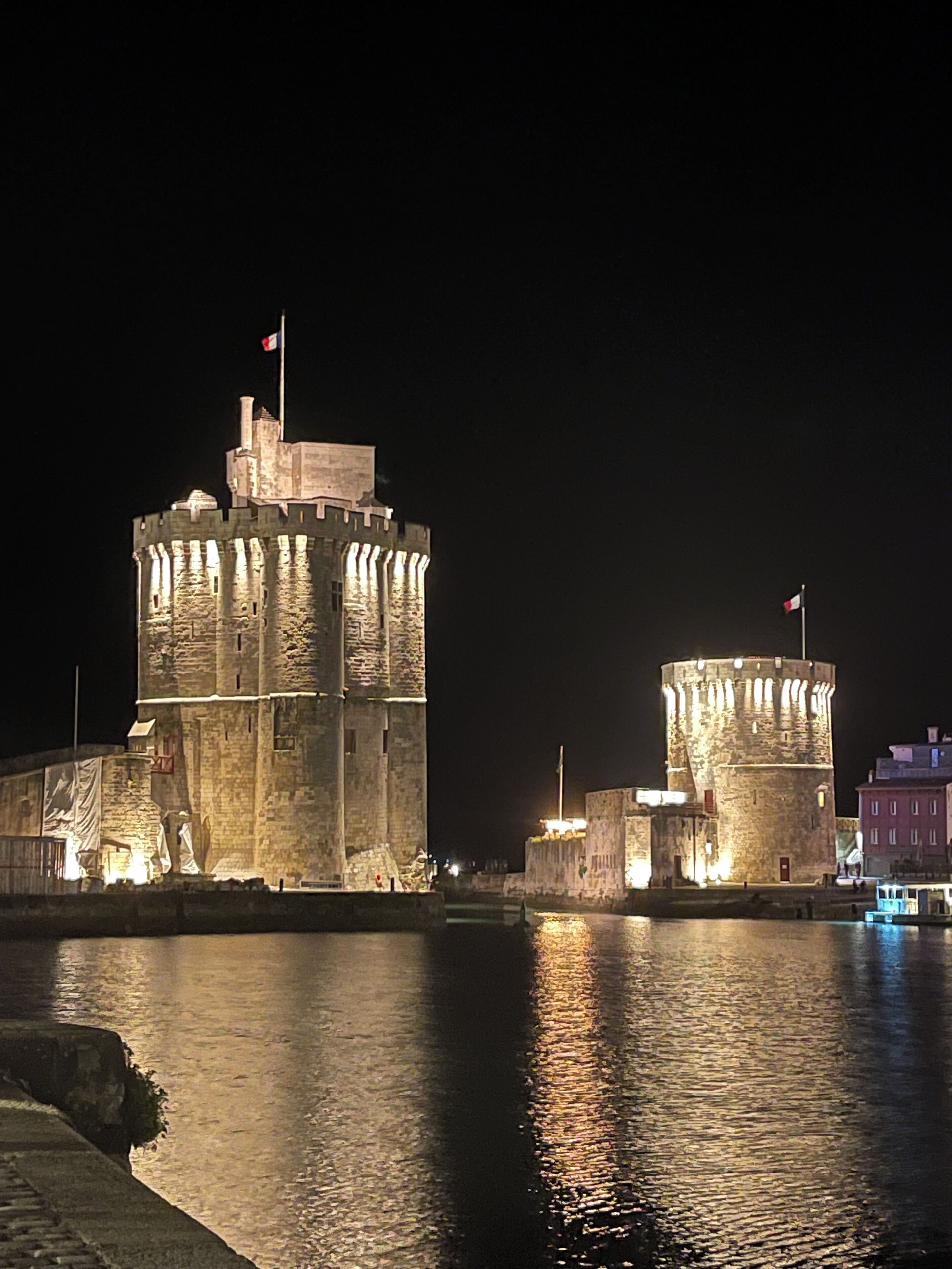 A historic stone castle with a flag, situated by a body of water at night.