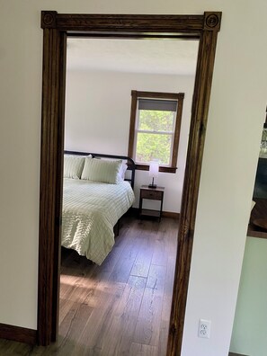 A bedroom with a bed, a nightstand, a window, and a wooden floor. - Cozy Sandhill Cottage, 15mi from Crystal Mountain, dog friendly, AC
(Elberta)