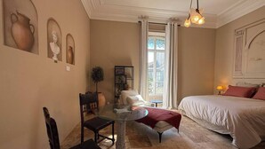 A bedroom with a bed, a glass table, a chair, and a small table with a plant. - To complete (Nîmes)