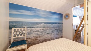 A bedroom with a beach mural, a white bed, a wooden chair, and a ladder leading to a loft. - Maisonnette, in the middle of the pines, 5 mn walk to the beach, near Hossegor (Seignosse)