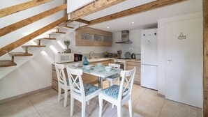 A modern kitchen with white cabinets, a wooden staircase, and a dining area with white chairs and a table. - Maisonnette, in the middle of the pines, 5 mn walk to the beach, near Hossegor (Seignosse)