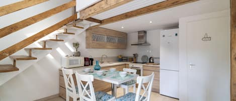 A modern kitchen with wooden beams, a dining table with chairs, and a white refrigerator.