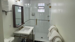 A bathroom with a white sink, mirror, and toilet. There is a shower area with a glass door and a towel rack. - Non-Smoking King/Queen With Balcony - NKQB (Manitou Springs)