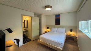 A bedroom with a bed, bedside tables, a desk, a chair, a bathroom with a mirror, and a window. - Non-Smoking King/Queen With Balcony - NKQB (Manitou Springs)