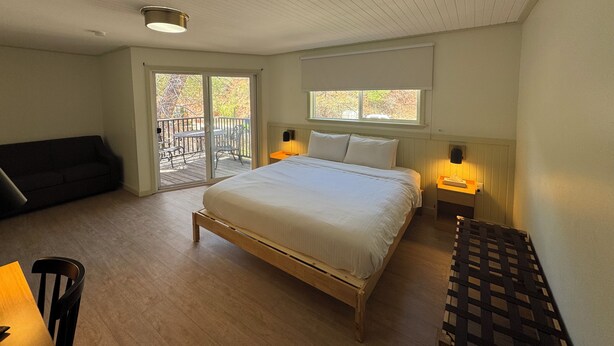 A bedroom with a large bed, a sofa, a dining table, and a balcony with a view of trees. - Non-Smoking King/Queen With Balcony - NKQB (Manitou Springs)