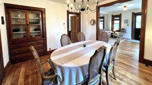 Ein Esszimmer mit einem runden Tisch, Stühlen, einer Kronleuchter und einer Holzkommode.