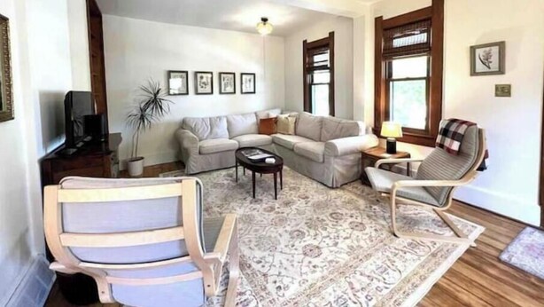 Ein Wohnzimmer mit einer Couch, Sesseln, einem Couchtisch, einem Teppich und einem Fernseher.