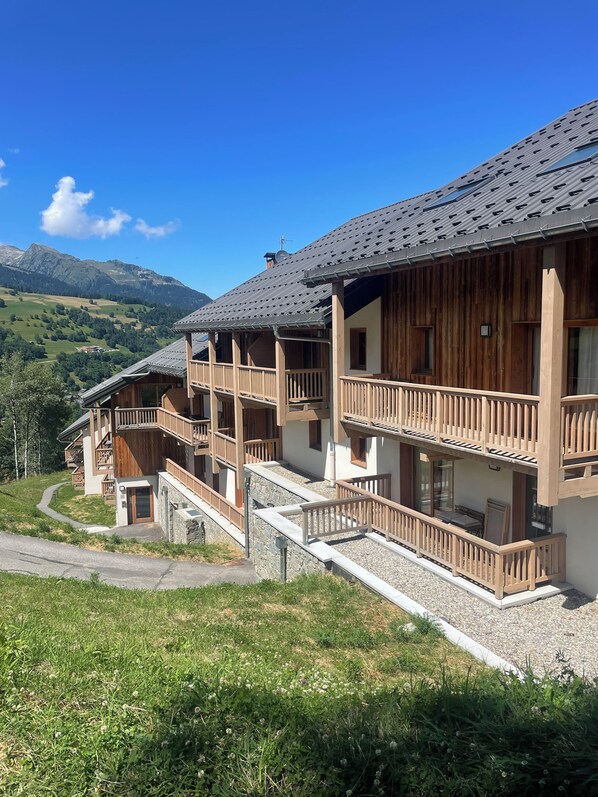 Un chalet à plusieurs étages doté de balcons en bois, d’un chemin de pierre menant à l’entrée et offrant une vue sur les montagnes environnantes.
